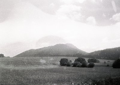 Vintage black-and-white landscape featuring rolling hills, sparse trees, and misty mountain peaks under diffused light. Mid-2...