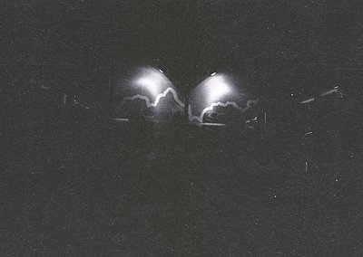 High-contrast black-and-white shot of two symmetrical, illuminated headlights against a dark background, likely from a vintag...