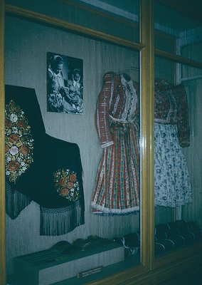Traditional folk costumes displayed in a museum vitrine, featuring embroidered vests, striped skirts, and headpieces with flo...