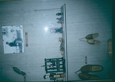 Vintage display case showcasing historical footwear and tools, likely from a museum or archive. Includes wooden clogs, a leat...