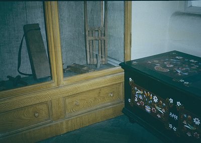 Vintage wooden furniture featuring a dark-stained dresser with brass handles and a floral-patterned trunk. Reflective mirror ...
