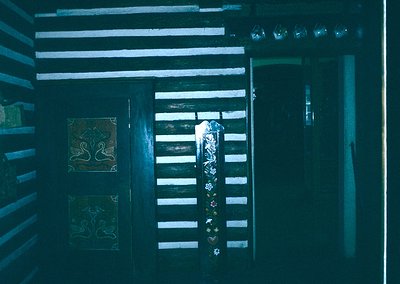 Dark, narrow wooden hallway with vertical slats, illuminated by a single dim light source. Decorative wall tiles featuring st...