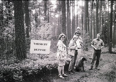 Family group photo in dense forest, 1960s Germany. Sign reads "VORSICHT DEPONIE" (Caution: Tip/Dump). Adults in mid-century a...