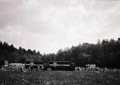 Vintage black-and-white photo of a vintage bus (likely 1950s–1960s) parked in a rural, wooded area with dense foliage. Group ...