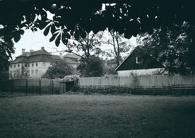 Vintage black-and-white photo of a European courtyard with a mix of residential and industrial elements. A two-story building...