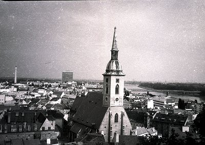 Aerial view of a historic European cityscape featuring a prominent **19th-century church tower** with a spire and clock, surr...