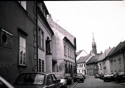 Vintage black-and-white street scene featuring Soviet-era cars parked along a narrow cobblestone alley. Prominent Soviet-era ...
