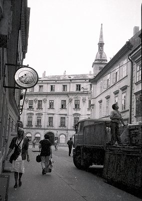 Classic European street scene featuring Baroque-style architecture with arched doorways and ornate facades. A vintage truck p...