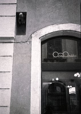 Sculpted stone bear head mounted above a curved doorway with Cyrillic sign "Оптика" (optics) in reflective glass. Architectur...