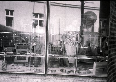Vintage black-and-white shot of a cluttered, multi-tiered display window showcasing household goods—pottery, textiles, and me...