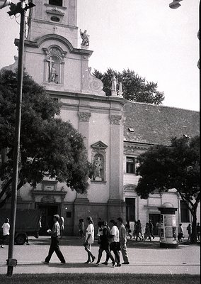 Neoclassical building façade with sculpted reliefs and a bell tower, likely from the early 20th century. Group of casually dr...