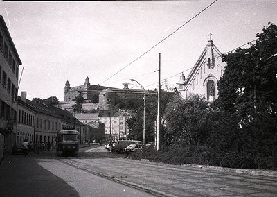Black-and-white street scene featuring a vintage bus and cars on a gently curving road, flanked by mid-20th century European ...