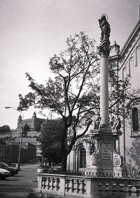 Historic stone fountain with Baroque-style statue of Virgin Mary and child atop, flanked by cherubs. Engraved plaque reads *"...