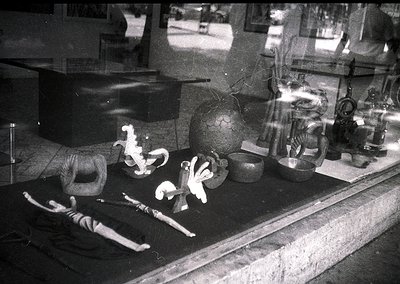 Vintage black-and-white display of vintage bicycles and ceramic items in a shop window. Two bicycles in mid-air, one with a r...