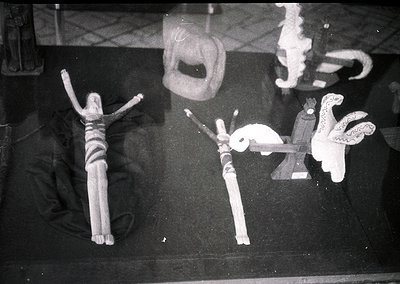 Vintage black-and-white photo of two wooden dolls in a crucifixion pose, flanked by a small ceramic bird and a decorative obj...