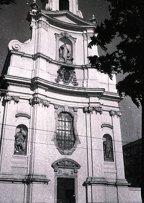 Baroque-style church façade featuring intricate stone carvings, including a central coat of arms and three relief sculptures ...