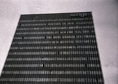 Mid-century Brutalist concrete panel wall with grid-like texture, likely part of institutional or public architecture. The ro...