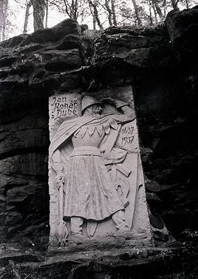 Relief sculpture of a robed figure holding a staff, carved into a rocky cliff face. Engraved inscription reads *"Jan Roháč z ...