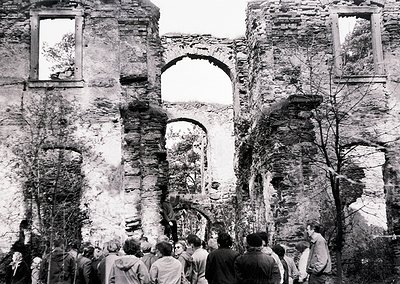 Ruins of a historic stone church with arched windows and crumbling walls, surrounded by a crowd of people. Architectural deta...