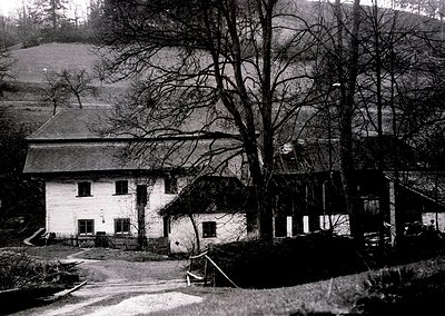 Two-story rural house with pitched roofs, surrounded by bare trees and rolling hills. Likely early-to-mid 20th century Alpine...