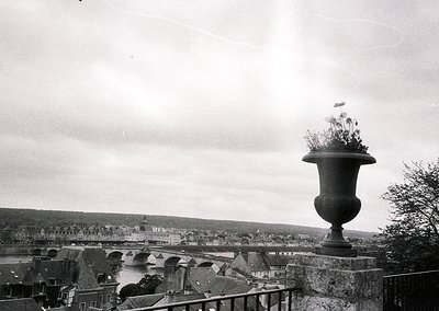 Vintage black-and-white shot of a large ornamental urn atop a stone balustrade, overlooking a river and historic town. Mid-20...