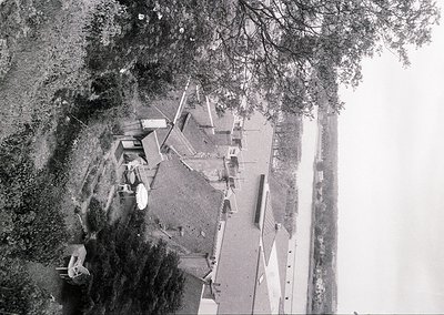 Aerial view of a coastal village with modest wooden structures and a narrow road. Dense greenery frames the scene, suggesting...
