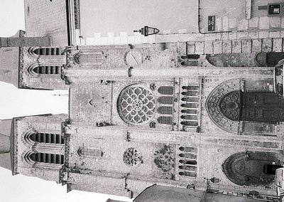 Aerial black-and-white view of a Gothic cathedral façade featuring a central rose window flanked by twin lancet windows and i...