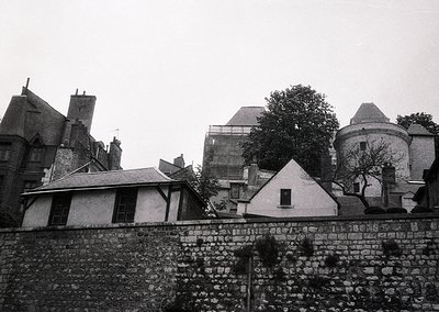 Historic European courtyard with stone walls and mixed-era architecture—19th-century brick buildings flank a central tower. O...