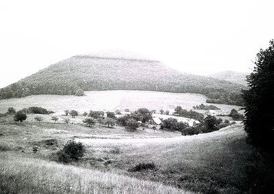 Vintage black-and-white landscape featuring a prominent artificial mound or hill, likely a burial tumulus, surrounded by open...