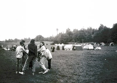 Group of four people in 1970s-style clothing—bell-bottoms, long sleeves, and layered scarves—standing in an open field surrou...