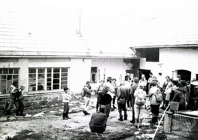 Group of people in 1970s-era outdoor setting, likely post-construction or cleanup. Brick building with large windows and conc...