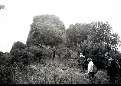 Black-and-white shot of hikers ascending a rugged rock formation, likely a historic fortress or natural landmark. Mid-20th ce...