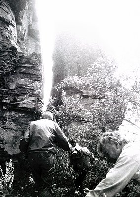 Two men engage in rock climbing in rugged terrain, mid-19th to early 20th century. One climber ascends a steep, moss-covered ...