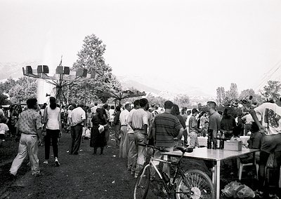 Crowded outdoor gathering in a rural setting, likely 1970s–1980s Eastern Europe. Central structure features a tall, multi-sid...