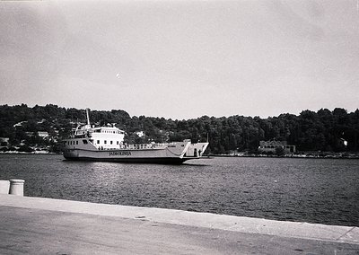 Mid-20th century ferry "Pardunlenia" navigating calm waters, likely a Bulgarian Black Sea route. Wooden pier and forested coa...