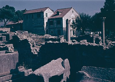 Blurred vintage photo of ancient ruins blending with modern structures—stone columns, fragmented marble, and a small water ba...