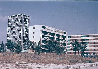 Mid-century Brutalist apartment blocks by a seaside dune, featuring raw concrete, geometric windows, and minimalist rooftop t...