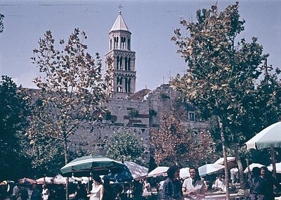 Historic bell tower with Romanesque arches dominates a bustling outdoor market in Split, Croatia. Stone architecture contrast...