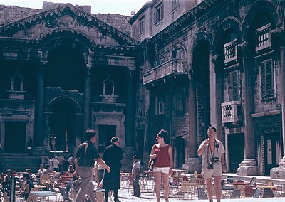 Roman Forum courtyard with ancient ruins and Renaissance-era balconies. Stone arches, columns, and weathered facades dominate...