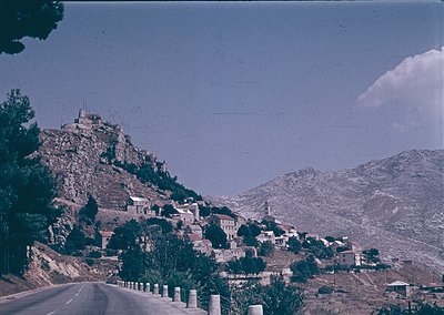 Vintage aerial-style view of a Mediterranean hillside village with terracotta-roofed houses nestled among rugged terrain. A w...