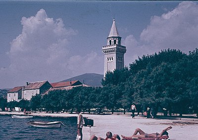 Vintage seaside scene featuring a prominent bell tower in the background, likely part of a historic coastal town. Mid-20th ce...
