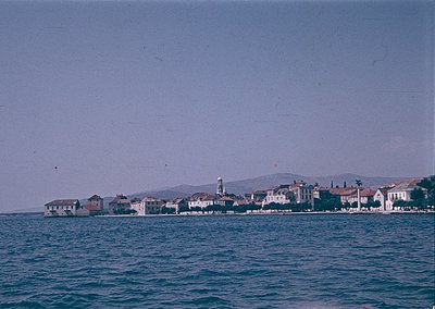 Vintage coastal town with low-rise buildings and a prominent lighthouse on a rocky outcrop. Waterfront architecture features ...