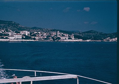 Coastal town nestled between deep blue waters and rolling hills, featuring clustered whitewashed buildings with red-tiled roo...