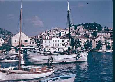 Classic wooden sailing vessel docked in a Mediterranean coastal town, mid-20th century. Whitewashed buildings with terracotta...