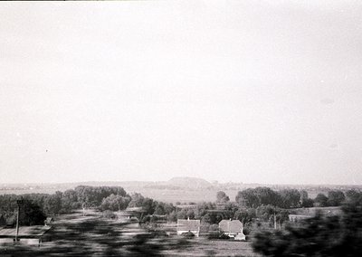 Vintage black-and-white rural landscape featuring scattered farmhouses, dense tree clusters, and open fields stretching to a ...