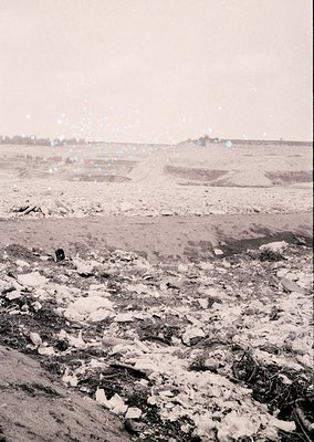 Barren, snow-dusted landscape with scattered debris and sparse vegetation, likely post-industrial or abandoned. Distant low-l...
