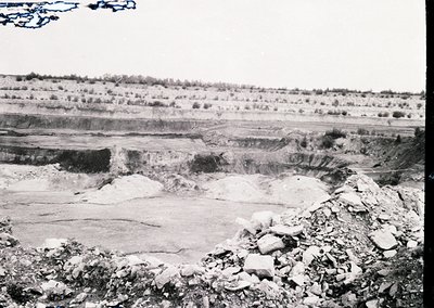 Mid-20th century open-pit mining site with exposed stratified rock layers, likely limestone or gypsum. Foreground shows loose...