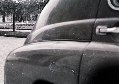 Close-up of a vintage car’s rear quarter panel, showing subtle scratches and minor paint imperfections. Blurred background re...