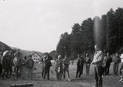 Mid-20th century group photo in rural setting, likely 1950s–1960s. Casual attire suggests informal gathering—men in trousers,...