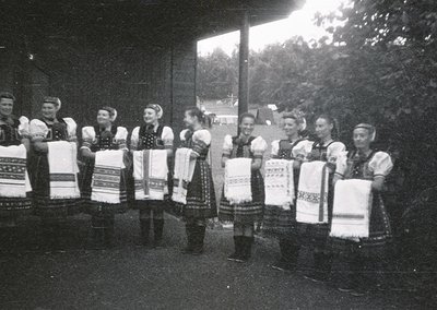 Group of women in traditional embroidered folk costumes, holding handkerchiefs with Cyrillic script, likely Bulgarian. Mid-20...